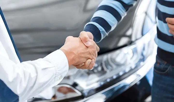 Käytetyn auton myyjä kättelee autoliikkeen ostajaa