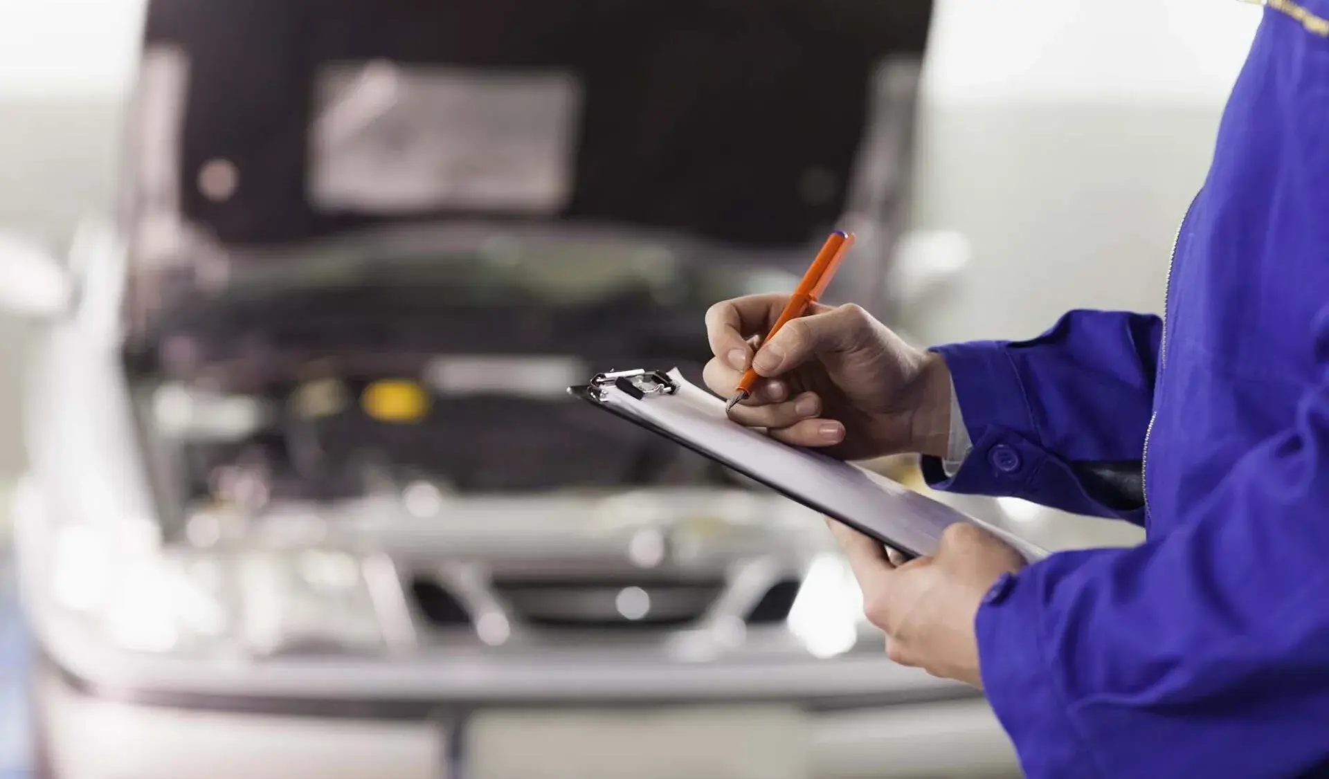 Automekaanikko korjaamolla kädessään auton huoltokirja