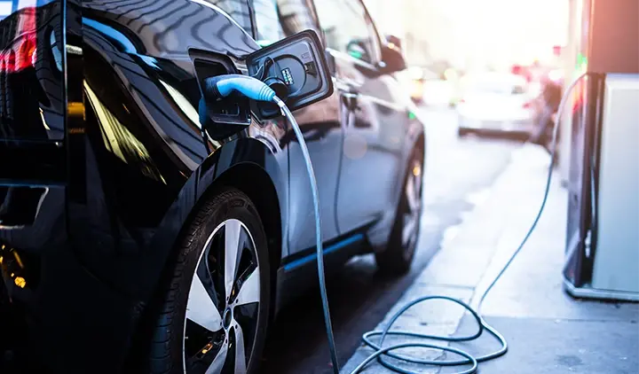 Musta sähköauto lataa latauspistokkeesta kadunvarressa
